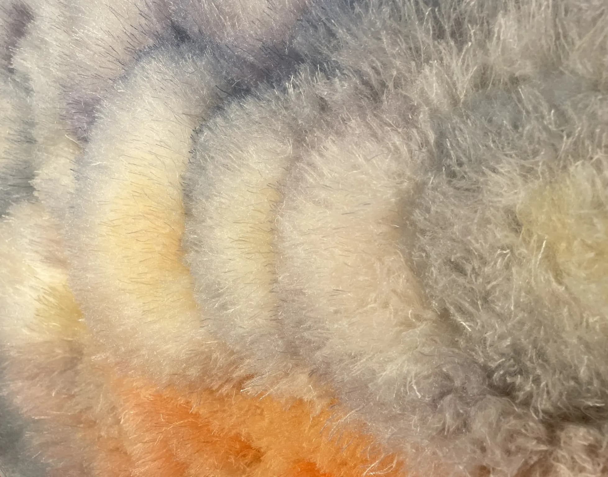 Close-up of a hand-tufted wool surface in warm amber and rust tones